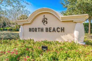 Ein Schild mit dem Aufschrift 'NORTH BEACH' und einem dekorativen Emblem, umgeben von einem angelegten Garten mit verschiedenen Pflanzen und Blumen.