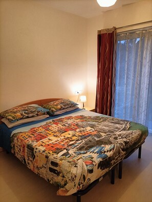Ein Schlafzimmer mit einem großen Bett, einem Nachttisch mit Lampe und einem Fenster mit Vorhängen.