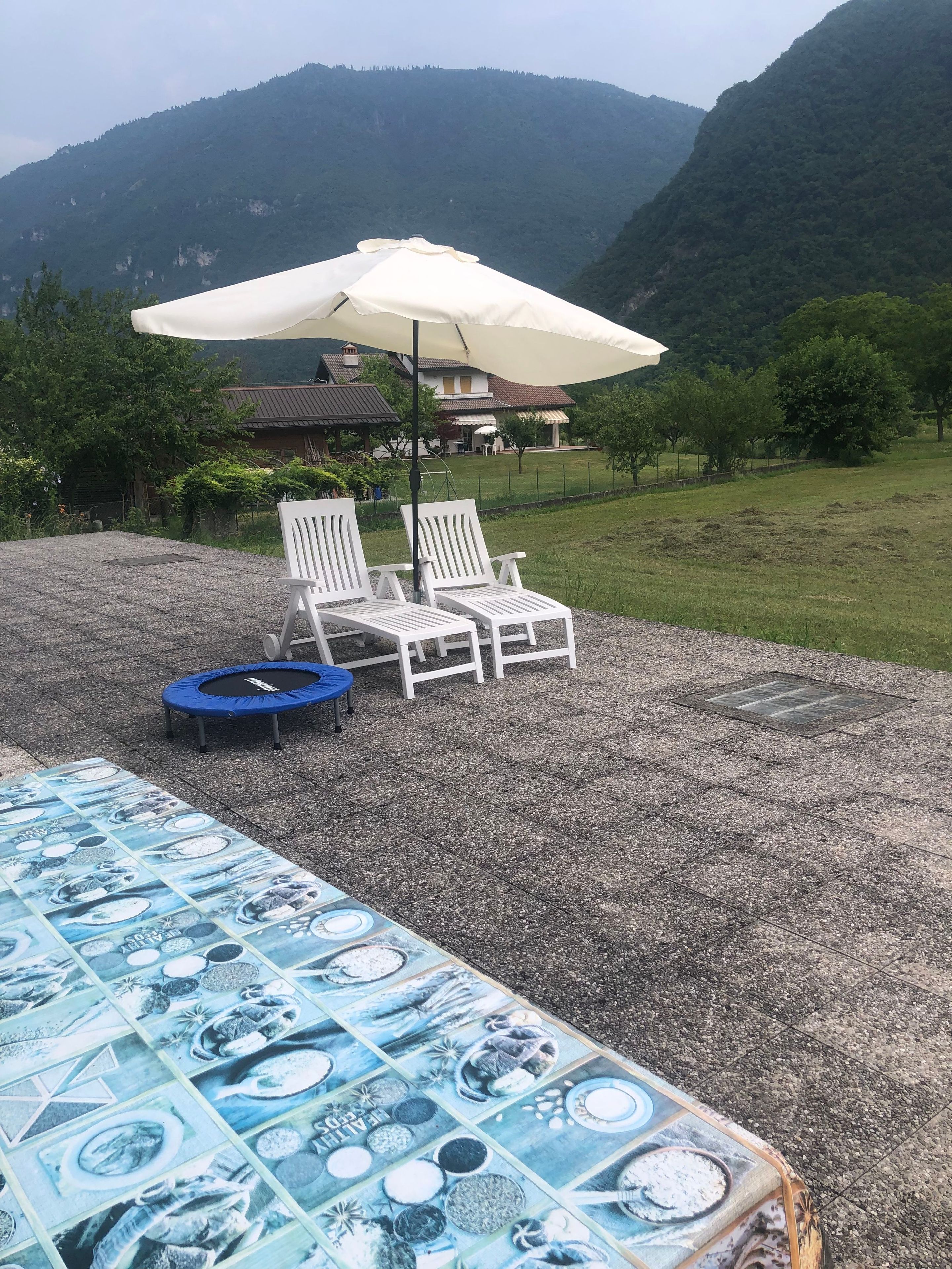 Eine Terrasse mit zwei weißen Liegestühlen, einem blauen Trampolin und einem Tisch mit blauer Tischdecke.