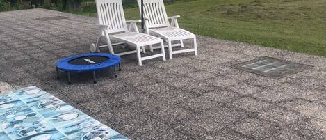 Un patio con dos sillones blancos, un trampolín azul y una mesa con mantel azul.