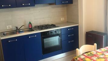 Eine kleine Küche mit blauen Schränken, einem Gasherd, einem Backofen und einer Spüle.