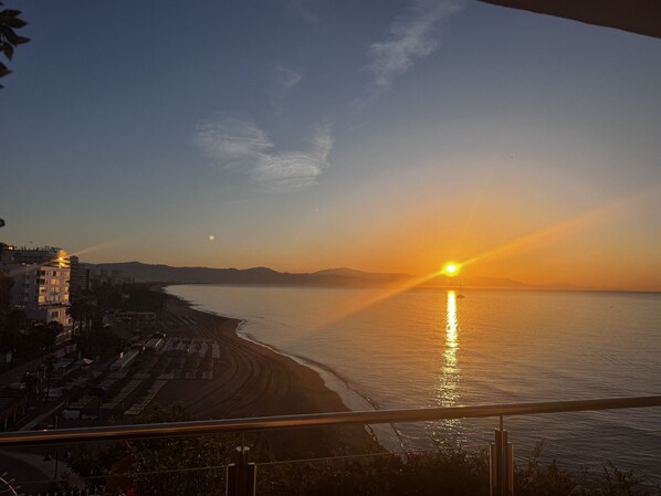 A coastal sunset view from a balcony overlooking a beach with buildings and a clear sky. - Modern Studio with Incredible Sea Views (Torremolinos)
