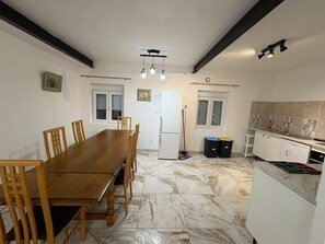 Een praktische keuken met een eethoek, met een houten tafel en stoelen, een koelkast en een betegelde spatwand.