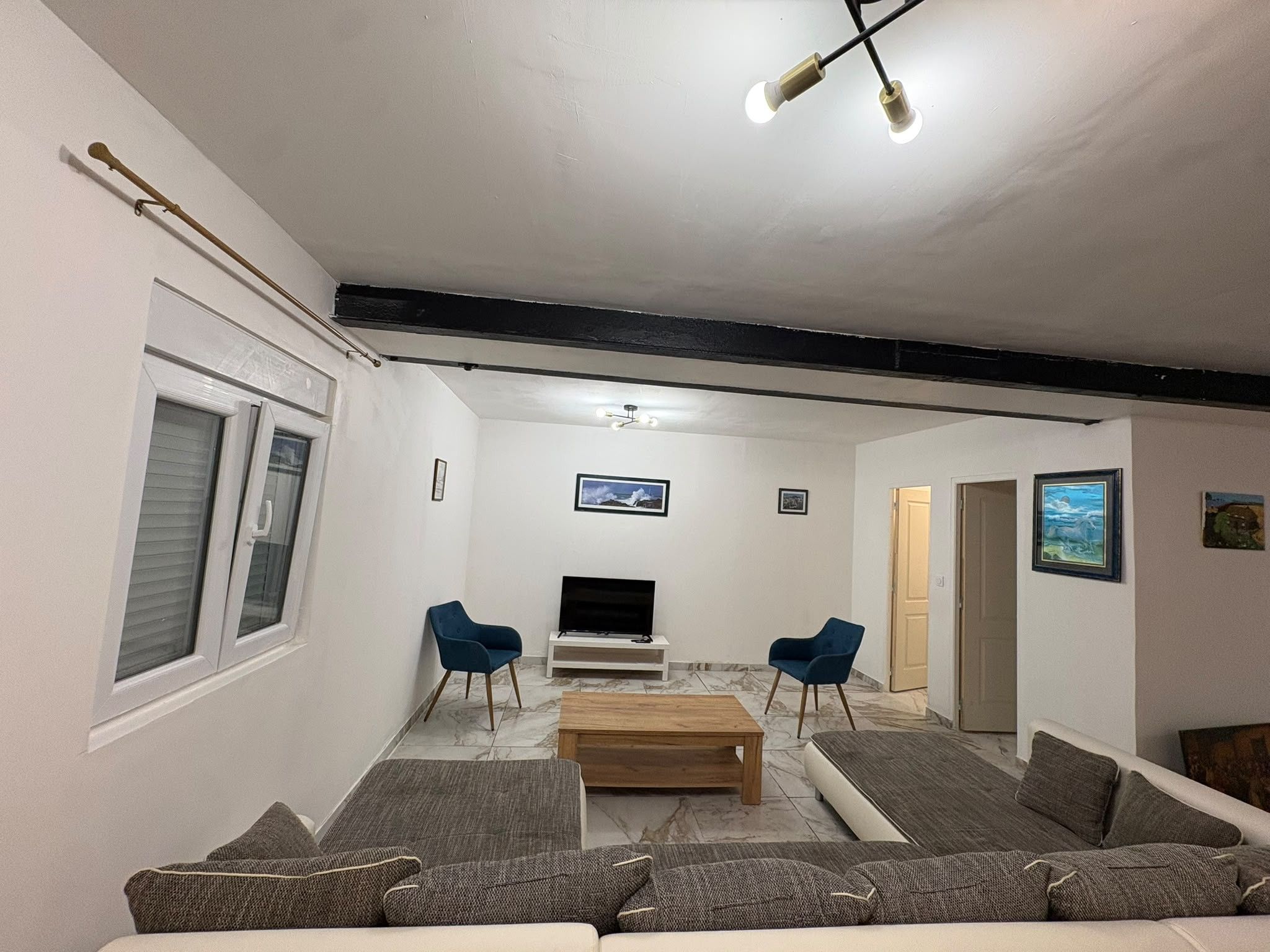 Sala de estar com sofá, duas cadeiras azuis, mesa de centro, televisão de tela plana e luminária no teto.