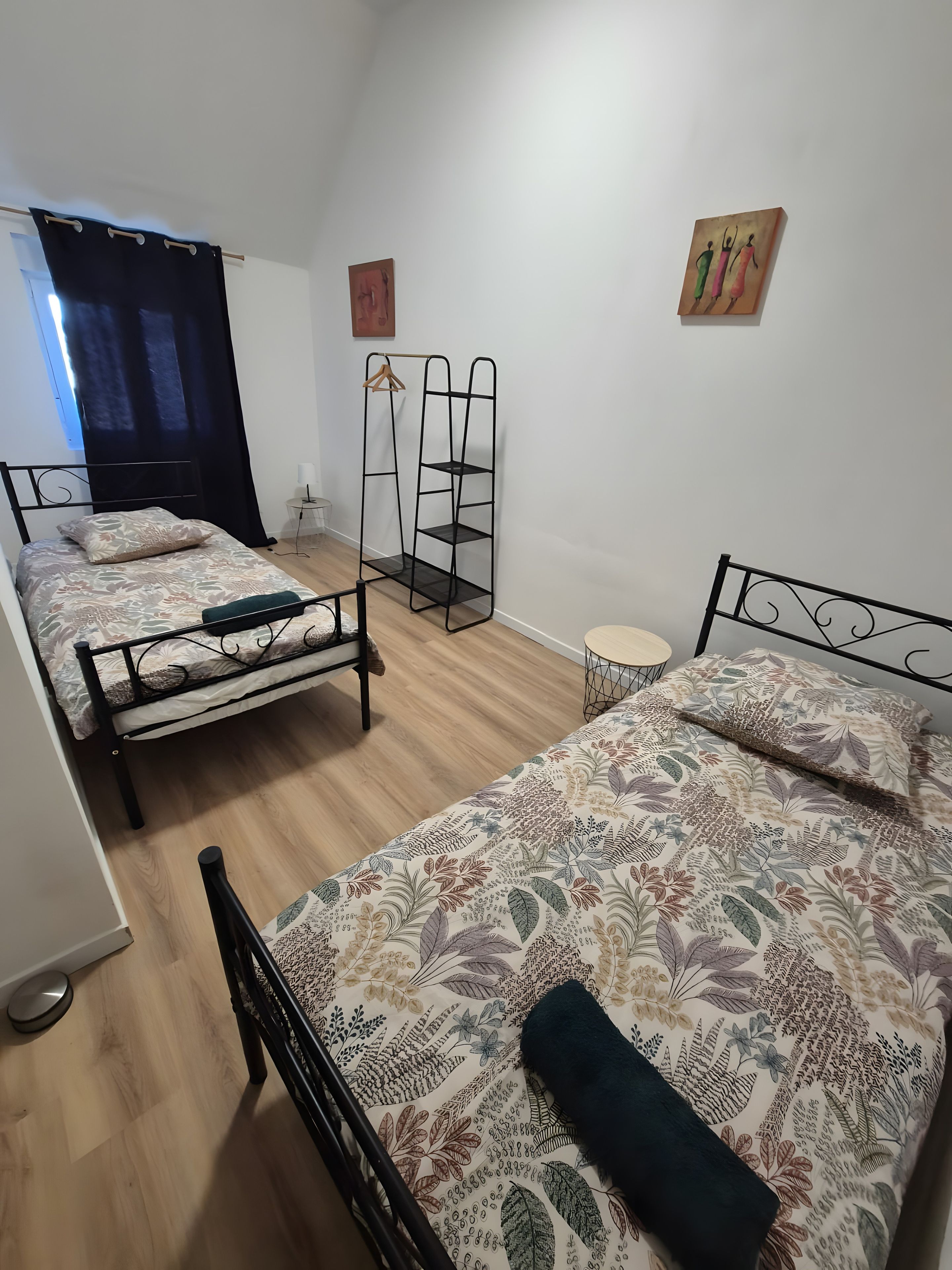 Ein Zimmer mit drei Einzelbetten, einem stehenden Kleiderschrank, einem kleinen runden Tisch und einem an der Wand befestigten Regal.