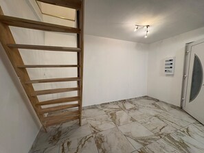 Een kamer met een houten trap, een plafondventilator en een deur met een raam.