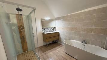 Een moderne badkamer met een douche in een glazen cabine, een vrijstaand bad en een houten wastafelmeubel.