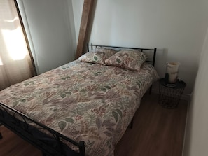 Una cama con una colcha y almohadas estampadas, una mesita de noche con una vela y una ventana con cortinas.