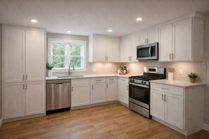 A modern kitchen with white cabinetry, stainless steel appliances, and a window providing natural light. - The Oak Park Casa Oasis | 6BR + Fireplace (Oak Park)