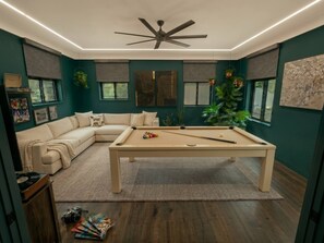 A room with a pool table, a beige sofa, and a ceiling fan. - The Oak Park Casa Oasis | 6BR + Fireplace (Oak Park)