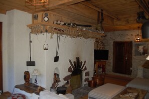 A rustic room with a stone wall, wooden beams, a fireplace, and various decorative items.