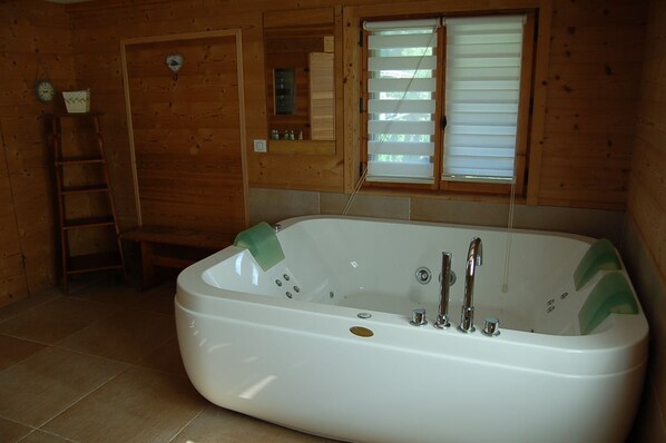 A bathroom with a freestanding bathtub, a wooden ladder, a window with blinds, and a clock on the wall.