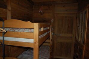 A wooden bunk bed with a mattress and a blanket, a door with a handle, and a small lamp on the wall.