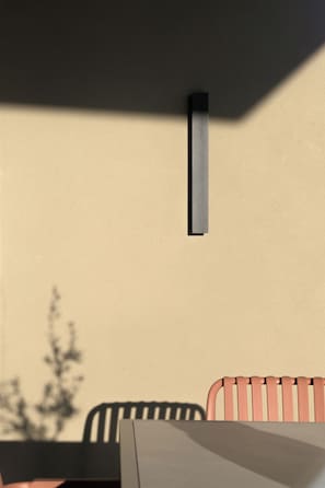 A room with a table and chairs, a wall-mounted light fixture, and a shadow of a tree. - Aelia Private Villa Triopetra (Unknown)