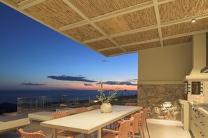 Un espace extérieur aménagé pour les repas, avec une table et des chaises, offrant une vue panoramique sur l’océan au crépuscule.