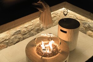 A glass-enclosed fire feature with logs, a glass candle holder, and a wine glass on a stone-tiled surface. - Aelia Private Villa Triopetra (Unknown)