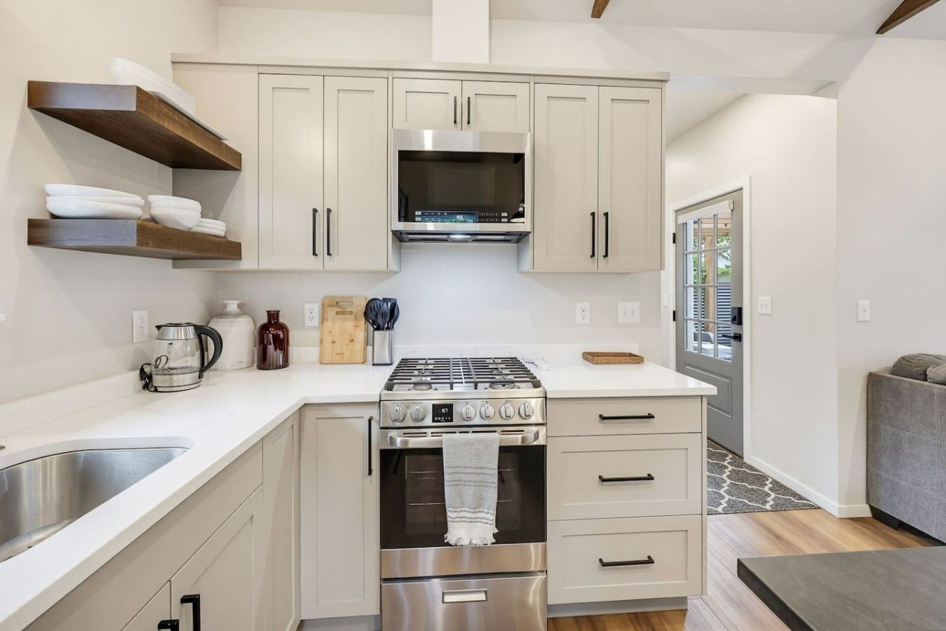 A compact kitchen with a gas stove, oven, and built-in microwave. There are wooden shelves above the counter and a window providing natural light.