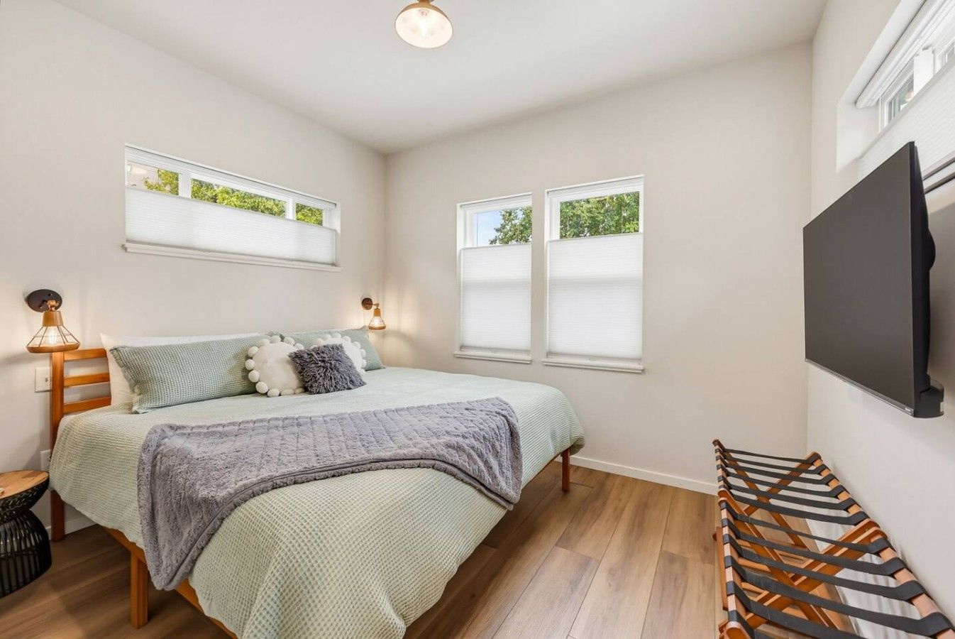 A bedroom with a bed, bedside lamps, a TV, and windows with blinds.