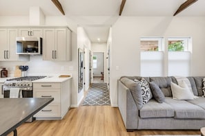 A modern kitchen with white cabinetry, a built-in oven, and a dining area with a wooden table. - Ashland Cottage | Walk to Downtown & Coffee (Ashland)