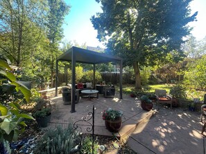 Un patio couvert aménagé avec du mobilier d’extérieur, entouré d’une végétation luxuriante et d’arbres.