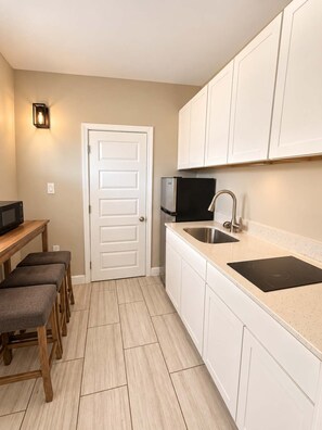 A compact kitchen with white cabinets, a stainless steel sink, a microwave, and a black induction cooktop. - The Sunny Seaside 300 Tenth | 102 (Myrtle Beach)