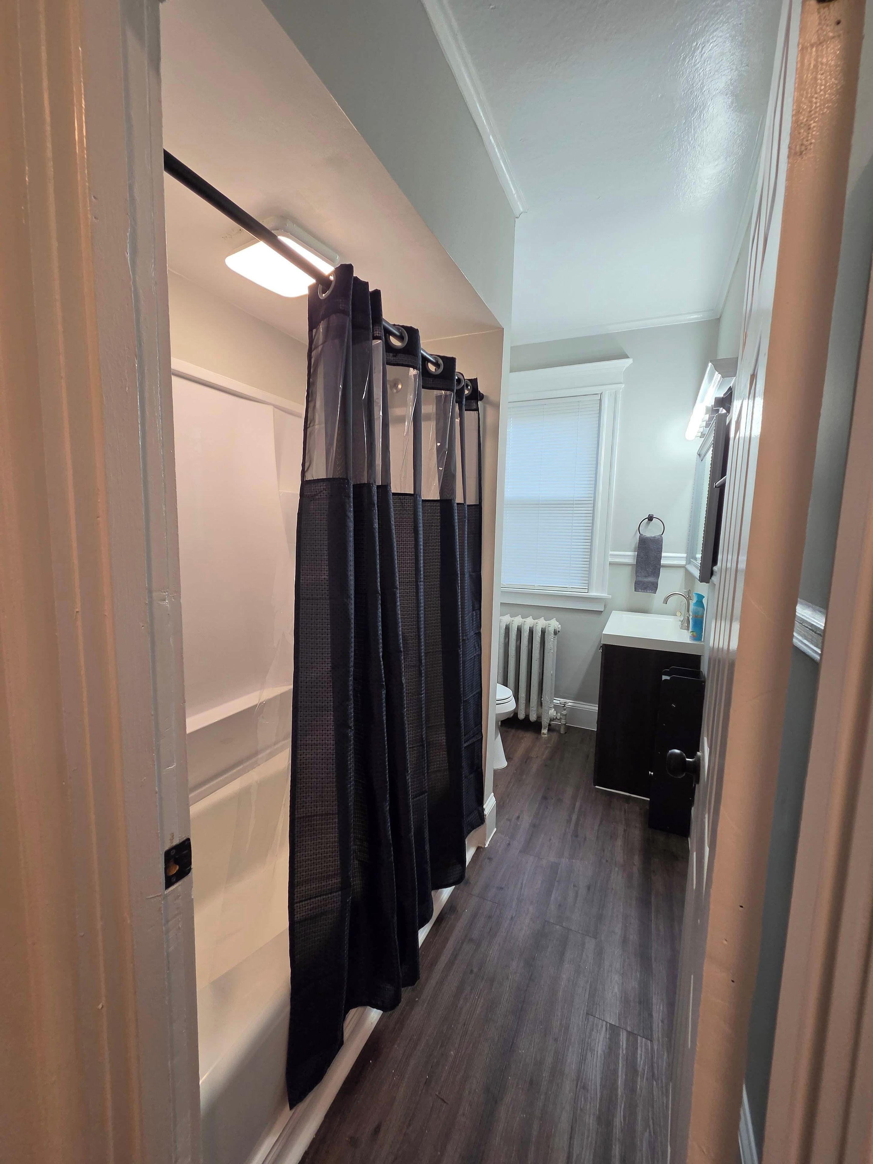 A narrow hallway with a shower curtain, a radiator, a sink, and a mirror.