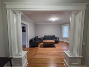 A spacious living room with a sectional sofa, a coffee table, and a dartboard on the wall. - 2BR Apartment Near Wesleyan 303 (Middletown)