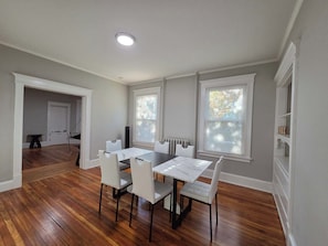 Un coin repas comprenant une table et des chaises, un radiateur et une fenêtre avec des stores.