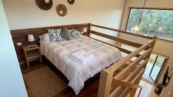 A modern bedroom with a wooden bed frame, a nightstand, and a bedside table. There is a window with a view of trees.