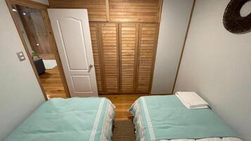A bedroom with two beds, a wooden wardrobe, and a door leading to another room.