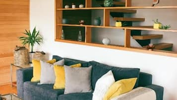 A modern living room with a dark blue sofa, a wooden bookshelf, and a glass coffee table.