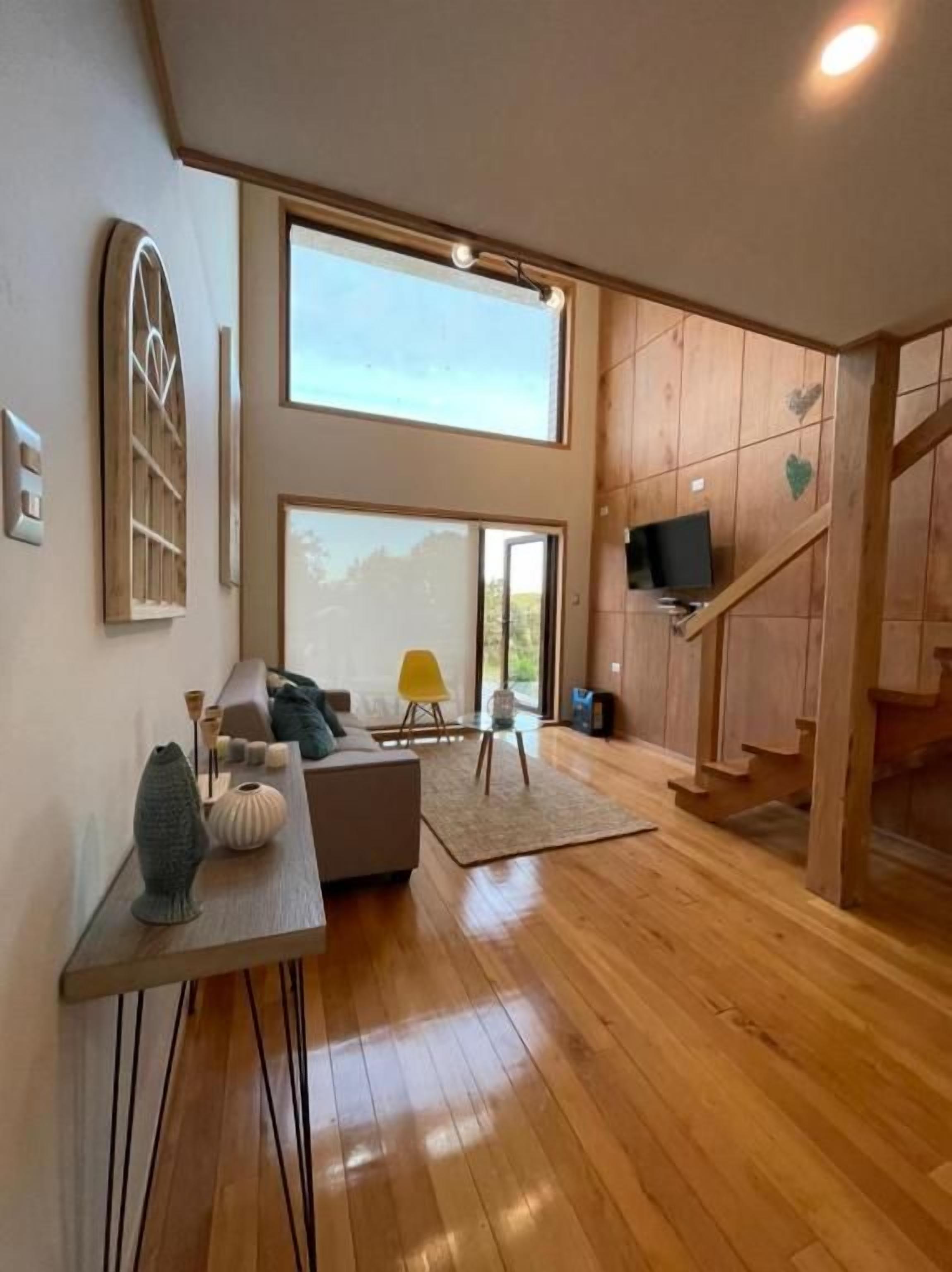 Una sala de estar moderna con un sofá, una mesa de centro y un televisor. Se ve una escalera que lleva a otro nivel.