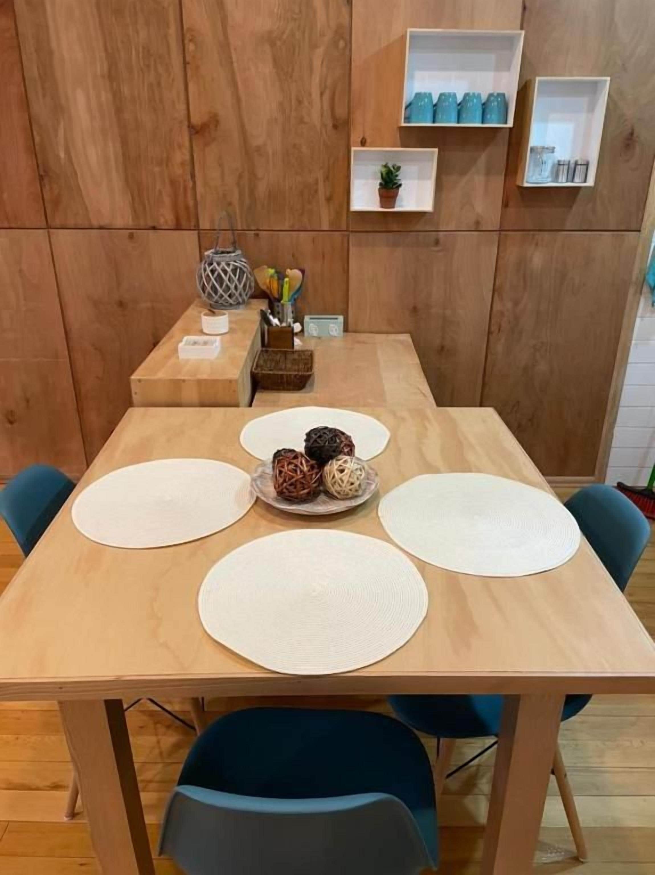 A wooden dining table with placemats, a bowl of decorative items, and blue chairs.