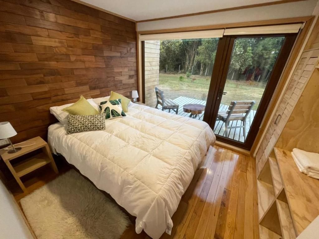 Un dormitorio con una cama grande, cabecera de madera, mesita de noche, lámpara y vistas a un patio exterior con sillas y una mesa.
