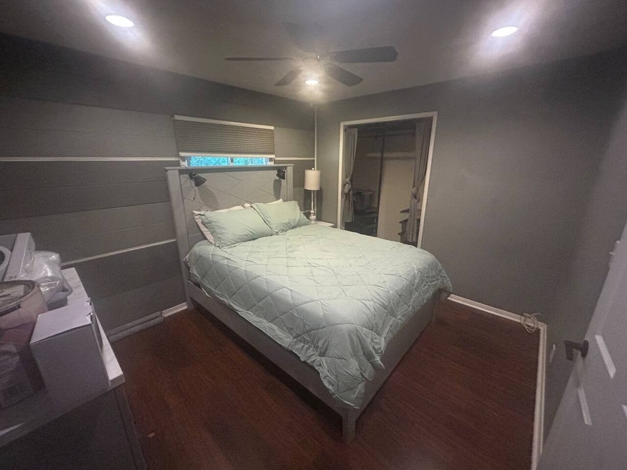 A bedroom with a bed, a desk, a ceiling fan, and a window with blinds.