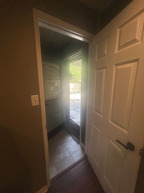Un couloir avec une porte fermée sur la droite et une porte entrouverte sur la gauche, donnant sur un balcon.
