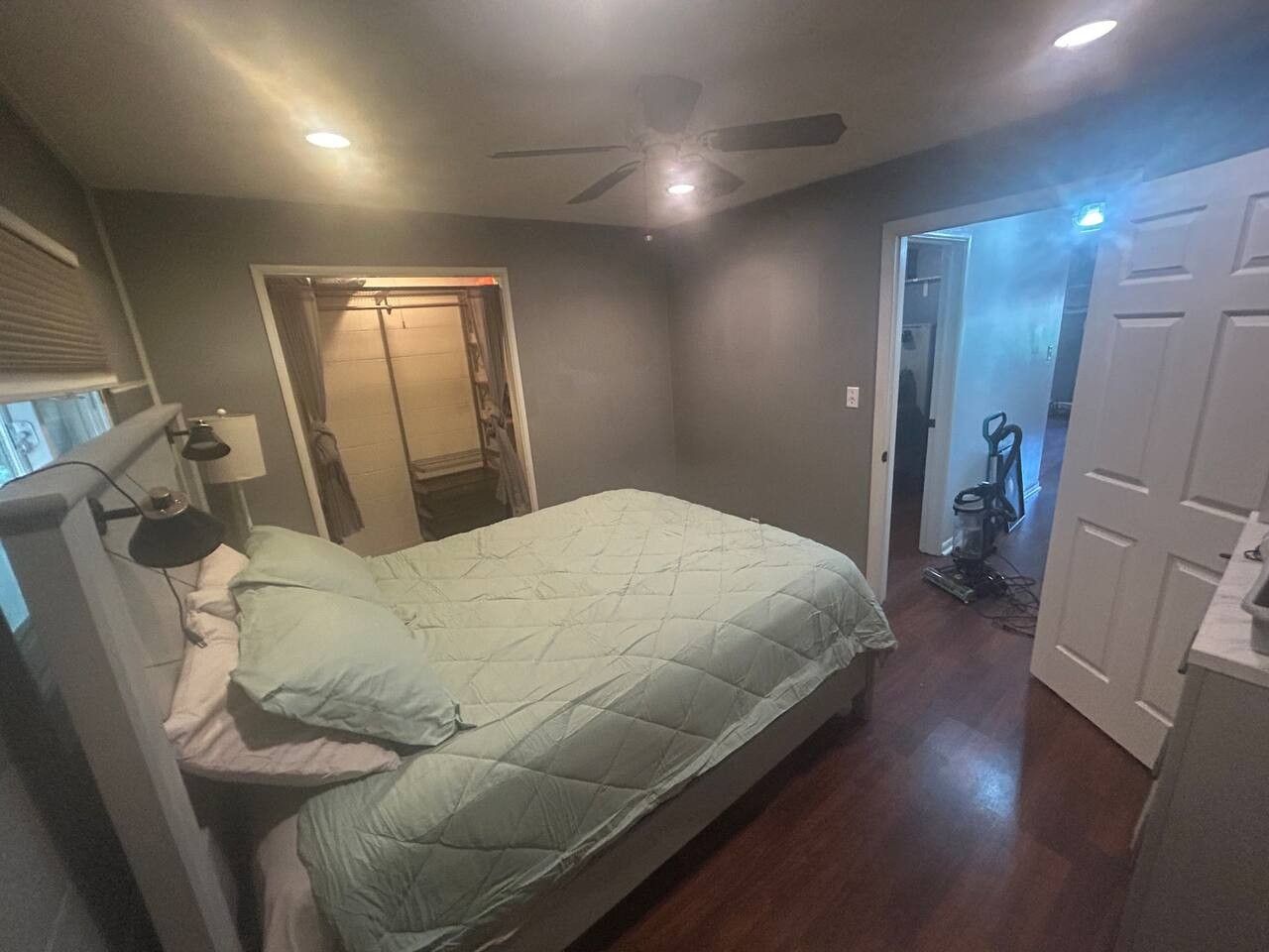 A bedroom with a bed, a ceiling fan, a door, and a hallway leading to a bathroom.