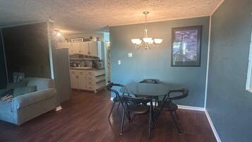 Un coin repas avec une table et des chaises, une cuisine à l’arrière-plan et un salon avec un canapé.