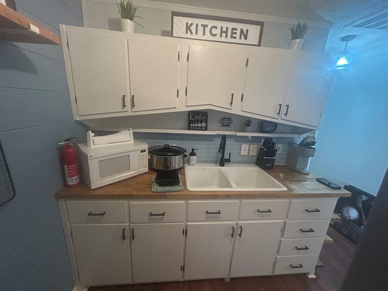 Une cuisine de taille réduite avec des meubles blancs, un four à micro-ondes, une cuisinière et un évier.