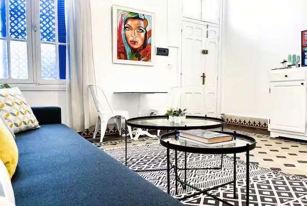 A room with a blue sofa, a round black coffee table, a white chair, and a painting on the wall. - La Marsa Vibe (Tunis)