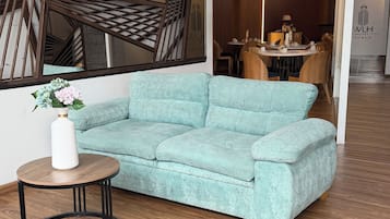 Een moderne hotelentree met een hoekbank, een ronde houten tafel en een decoratieve vaas.