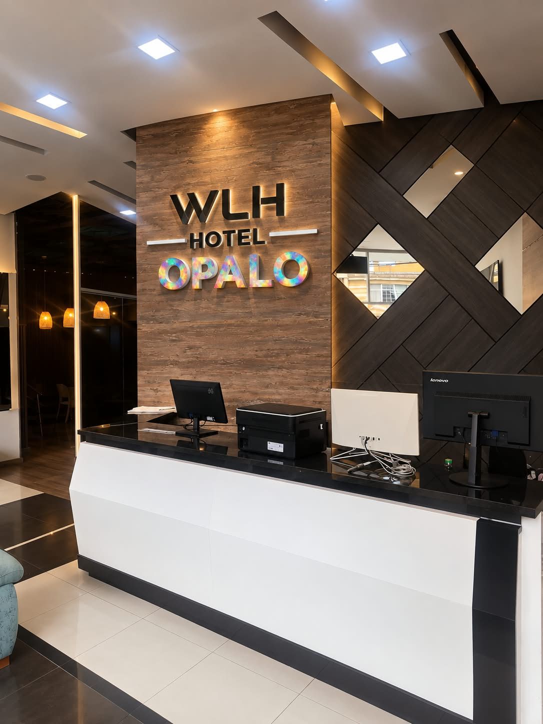 Een modern ingerichte hotelreceptie met een houten paneel en een digitaal scherm.