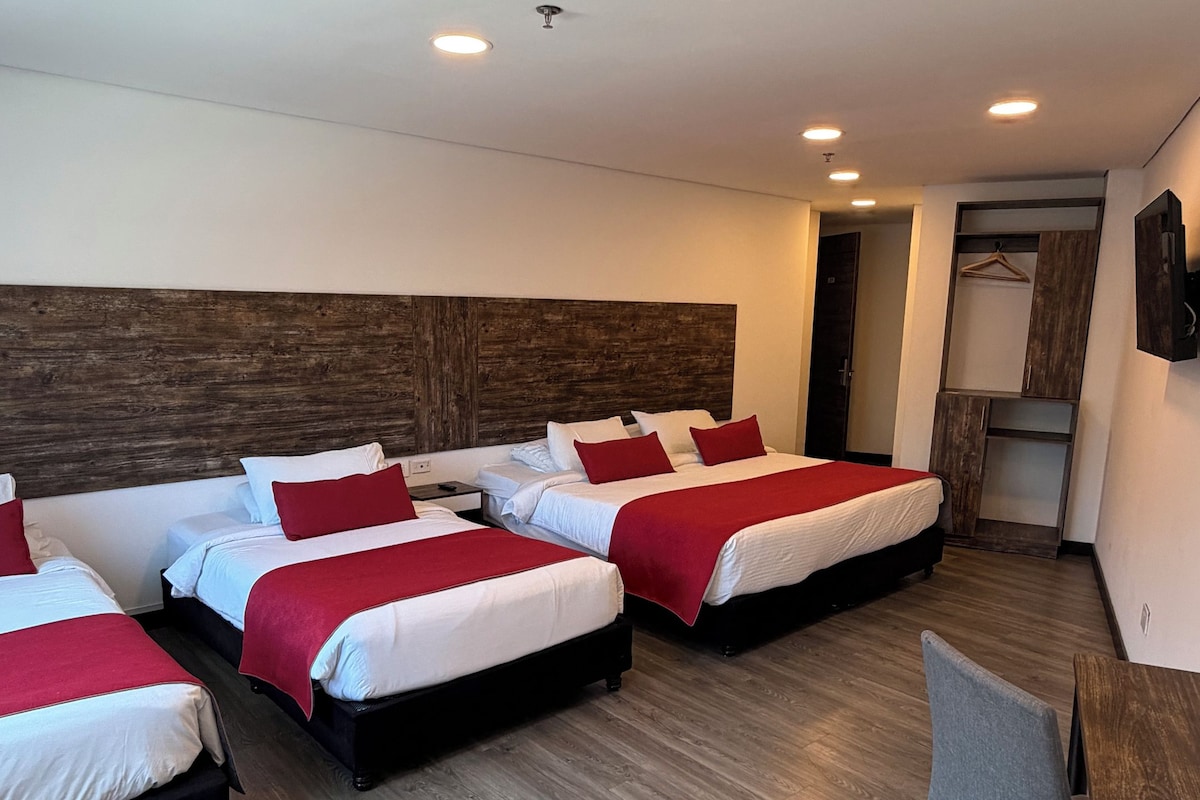 A hotel room with four beds, a desk, and a chair.
