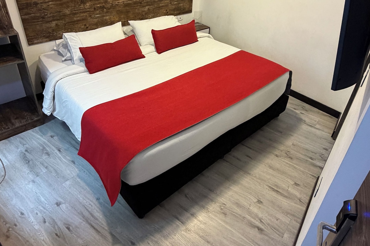 A modern hotel room with a large bed, a wooden headboard, and a flat-screen TV.