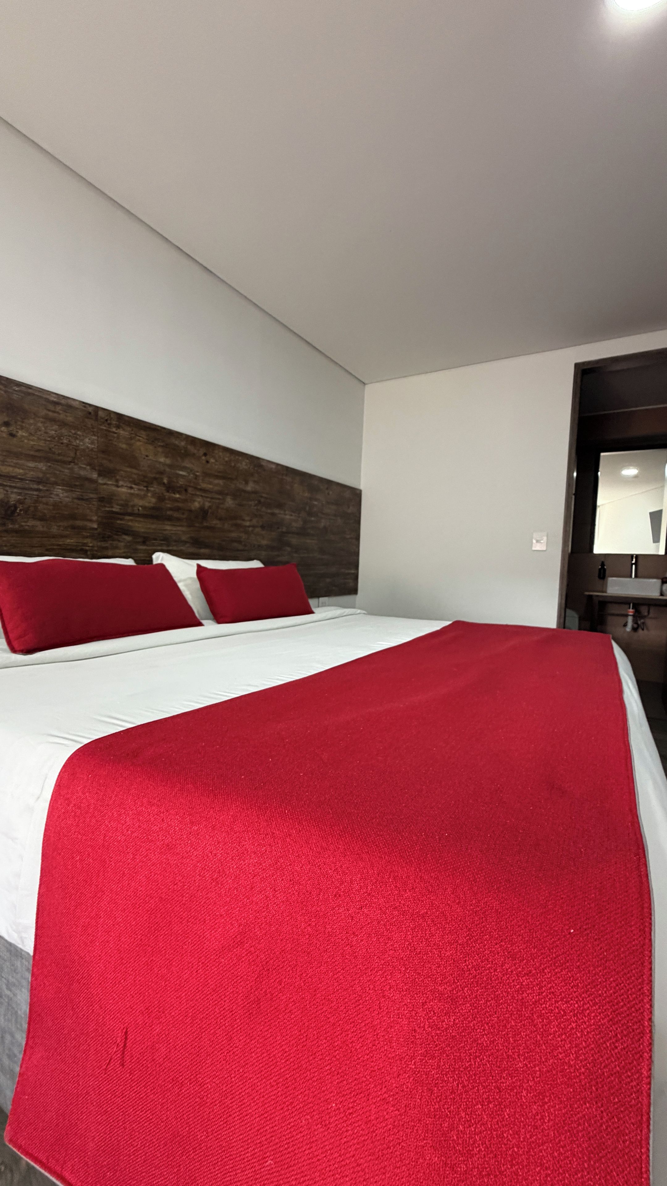 Een hotelkamer met een bed, rode kussens, een rode plaid, een houten hoofdbord en een spiegel.
