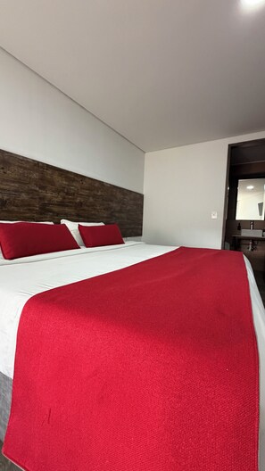A hotel room with a bed, red pillows, a red throw blanket, a wooden headboard, and a mirror. - Hotel WLH Ópalo (Bogotá)