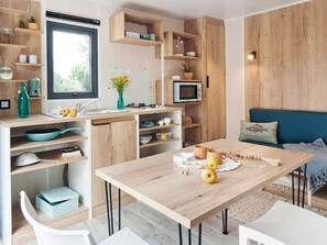 A modern kitchen with wooden cabinetry, a dining table, and a blue sofa. - Mobile home with AC, terrace - 4 guests (Grayan-et-l'Hôpital)