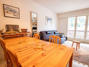 A cozy living room with a wooden dining table, a sofa, and a large window. - Spacious apartment at the foot of ski slopes - 8 guests (Villarodin-Bourget)