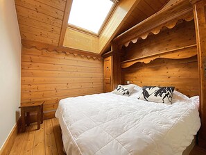 Ein Schlafzimmer mit Holzboden, einem Oberlicht, einem Bett mit weißer Bettwäsche und einem kleinen Holzschemel.
