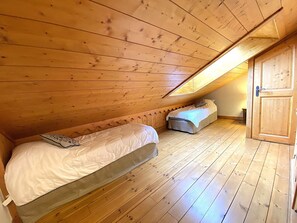 A small, wooden-paneled attic bedroom with two beds and a sloped ceiling. - Comfortable apartment mountain view - 8 guests (Méribel)